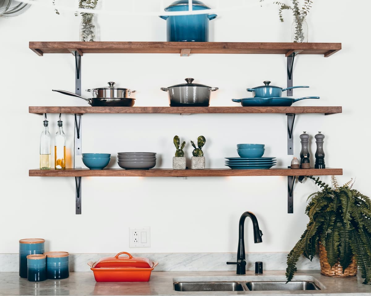 Open kitchen shelves with pots, pans, bowls and plates above a sink